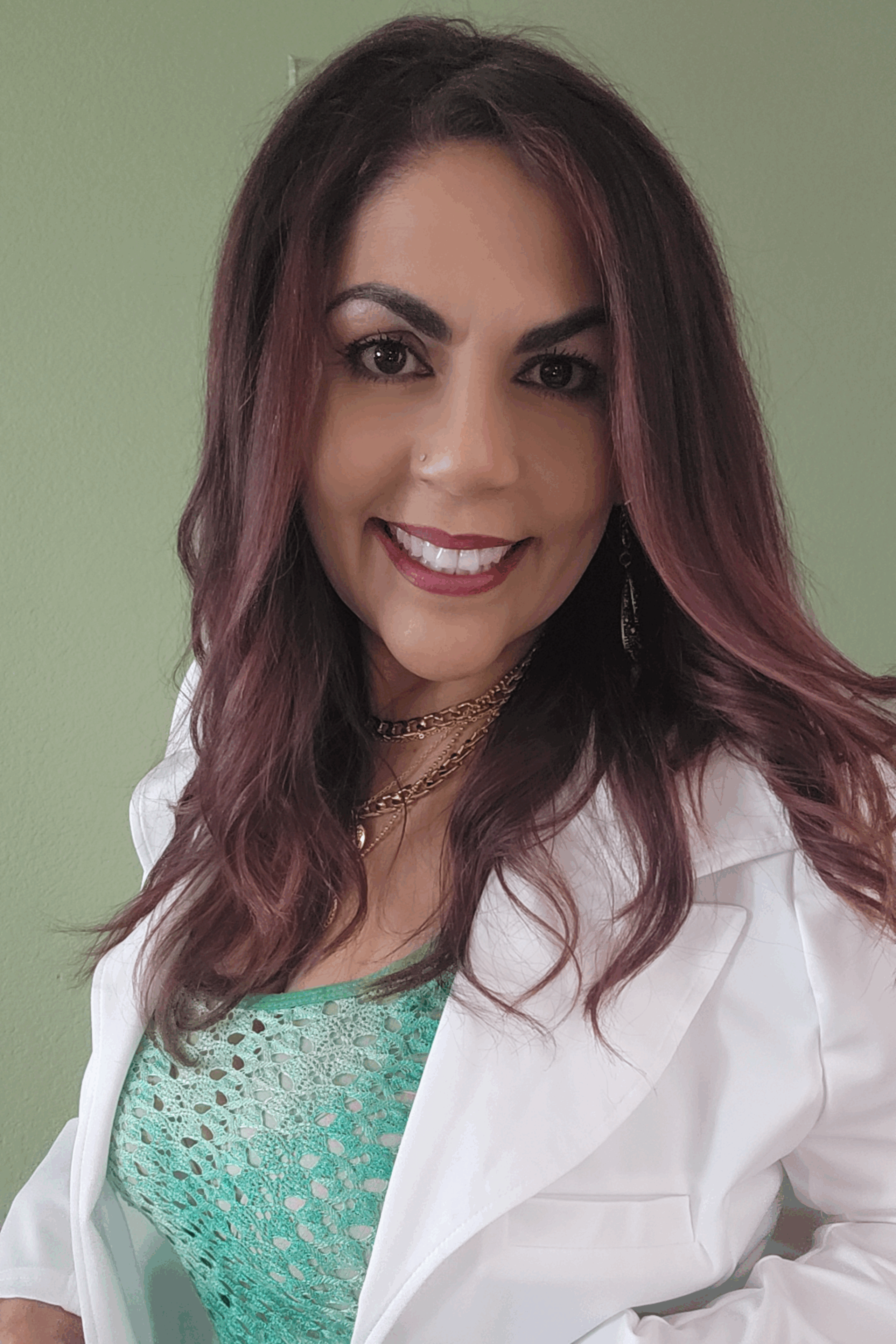 Smiling woman with long hair wearing a white coat and green top.